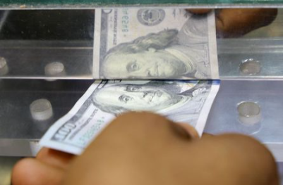 A man inserts a U.S. dollar banknote into the window of a local currency exchange in Aden, Yemen June 29, 2021. Picture taken June 29, 2021. REUTERS/Fawaz Salman